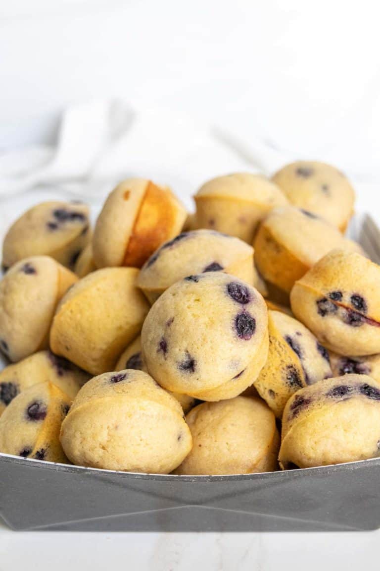 A rectangular tray filled with a stack of mini blueberry muffins on a white surface.