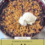 A skillet of warm berry crisp, topped with a scoop of vanilla ice cream, sits on a light-colored cloth.