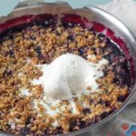 A round pan of berry crisp topped with a scoop of melting vanilla ice cream. The text above reads "Mixed Berry Crisp.