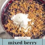 A pan of berry crisp topped with oat and pistachio crumble and two scoops of vanilla ice cream, placed on a beige cloth.