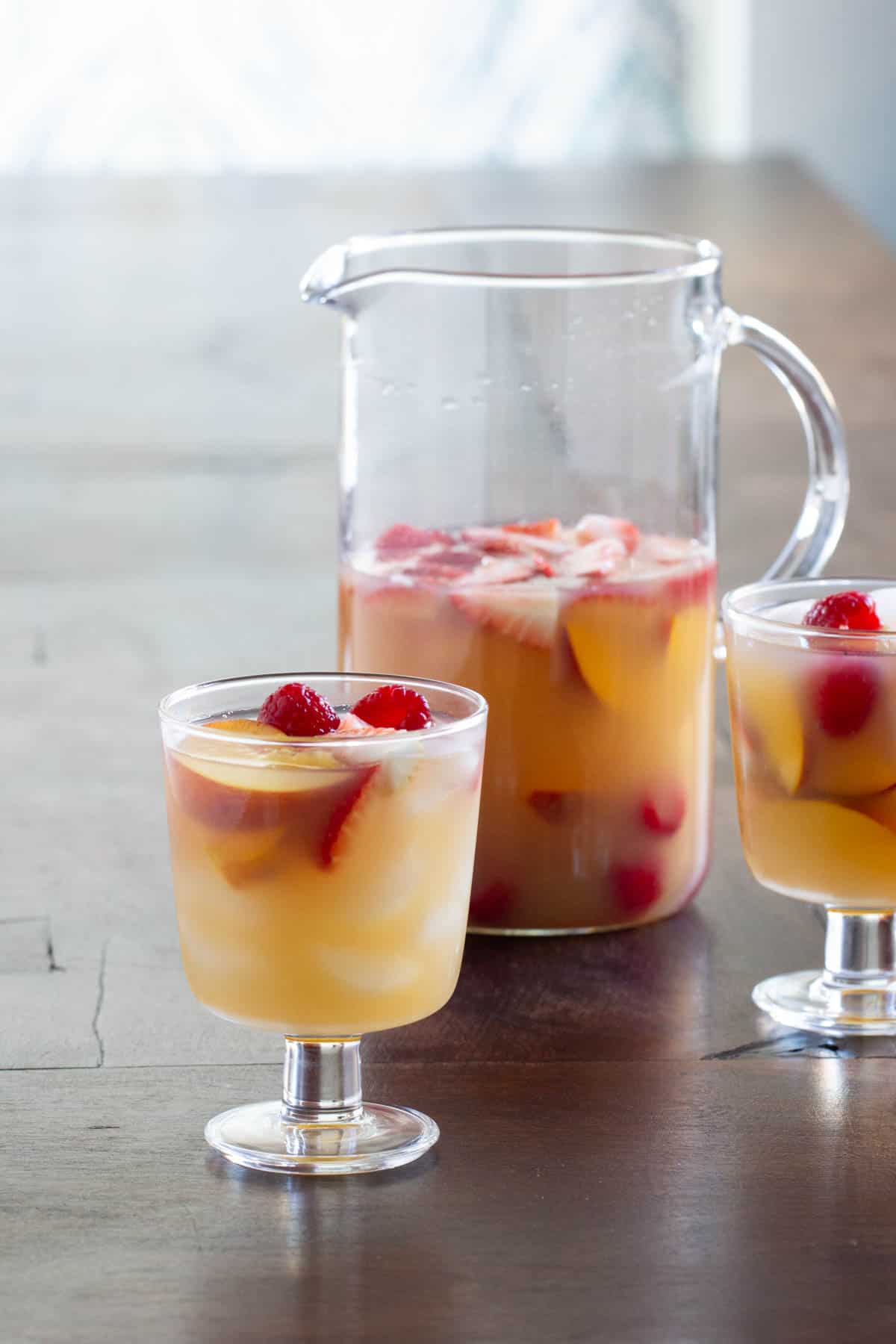 A pitcher and two glasses filled with fruit-infused sangria on a wooden table.