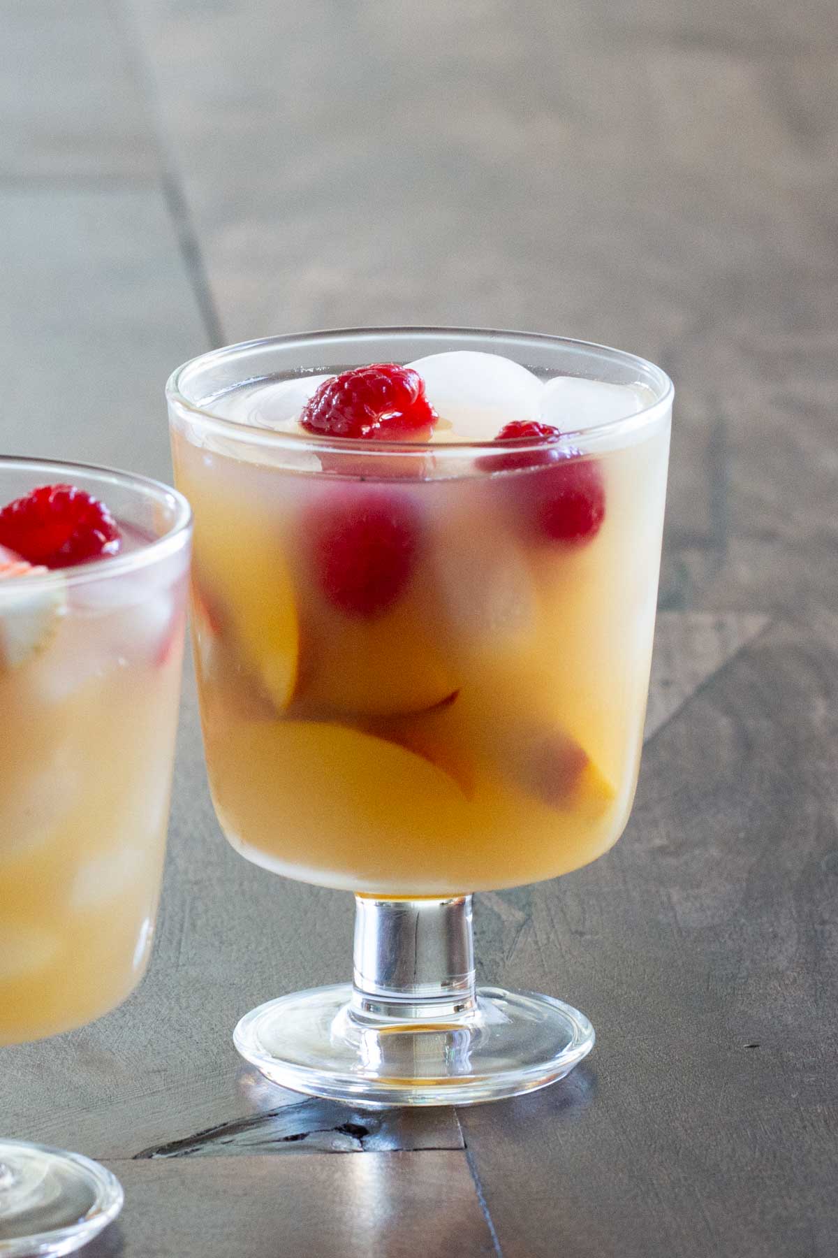 A glass of sangria with diced fruit and red cherries, served on a smooth surface.
