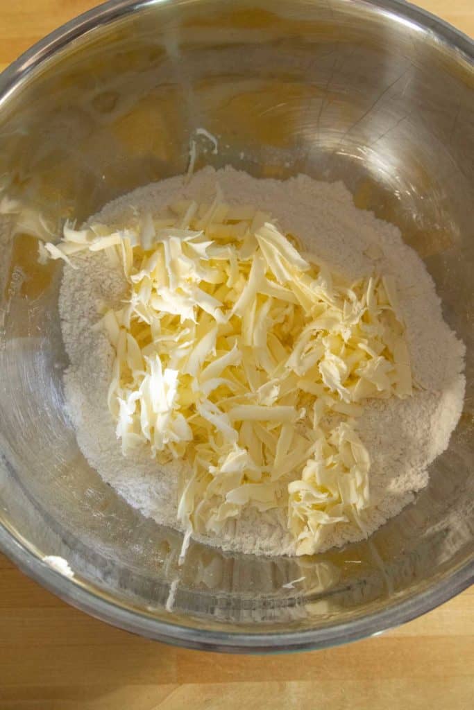 A stainless steel bowl containing flour and shredded butter, ready for mixing on a wooden surface.