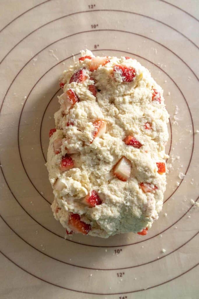 A ball of freshly made strawberry biscuit dough positioned on a circular baking mat marked with diameter measurements.