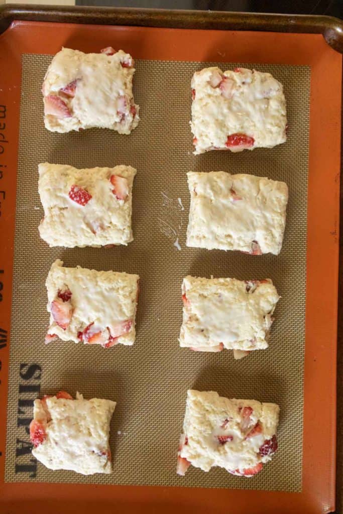 Six pieces of raw strawberry biscuit dough arranged on a silicone baking mat.