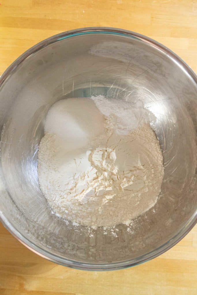 A glass bowl containing a mixture of flour and sugar on a wooden surface, ready for baking.