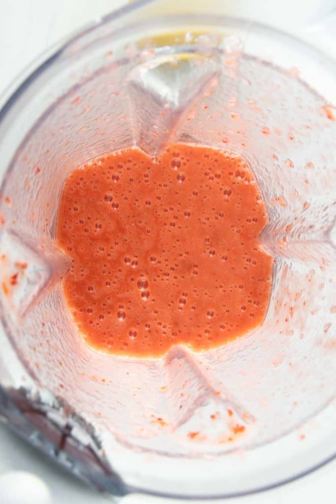 Top view of a blender with freshly blended strawberry sauce showing its smooth texture and vibrant red color.