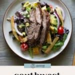 A plate of southwest salad topped with grilled steak slices, cherry tomatoes, black beans, crispy tortilla strips, and fresh mixed greens.