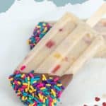 A delicious banana popsicle with visible fruit pieces is partially dipped in chocolate and topped with colorful sprinkles, making it a fun twist on classic banana popsicles.