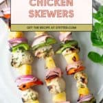 Chicken skewers grilled to perfection with bell peppers, pineapple, and red onions are served on a white plate.
