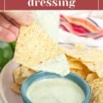 A hand dips a tortilla chip into a bowl of jalapeño ranch dressing, with more chips and a colorful napkin in the background.
