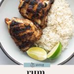A plate with two pieces of jerk chicken, a serving of white rice, and two lime wedges. "Rum jerk chicken" text and a logo appear at the bottom.