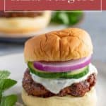 A delicious lamb burger topped with cucumber, red onion, and white sauce on a bun, served on a plate with a mint garnish—perfect for fans of tasty lamb burgers.
