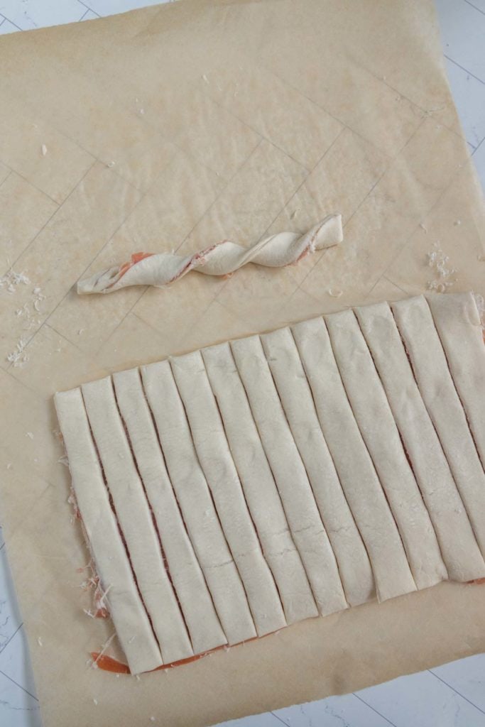 Puff pastry strips are laid out on parchment paper, one strip is twisted.