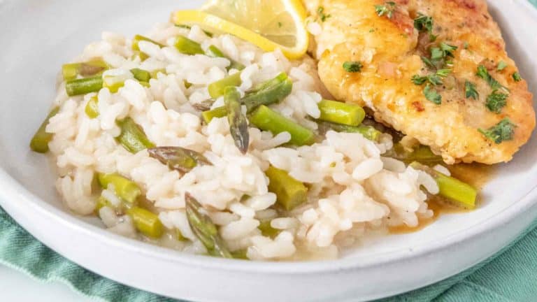 Plate with asparagus risotto and a piece of breaded chicken garnished with chopped herbs and a lemon wedge.