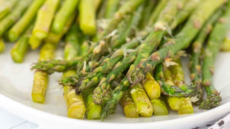 A white plate with a pile of cooked asparagus spears, displaying a green hue and tender texture.