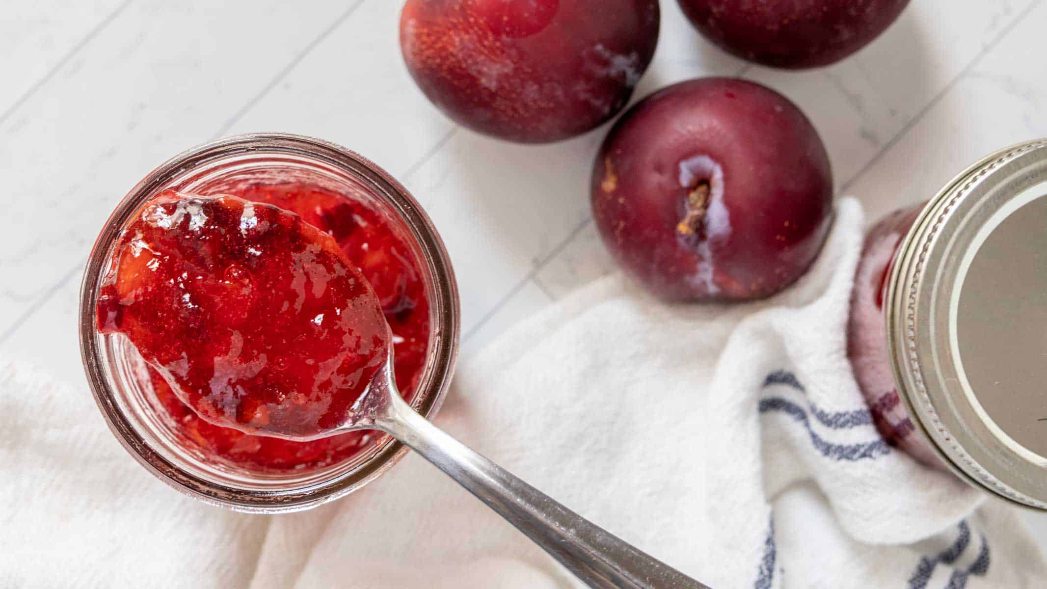 Overhead view of a spoon lifting plum jam from the jar.