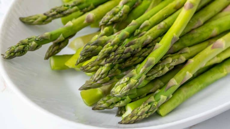 A close-up of fresh green asparagus spears piled on a white plate.