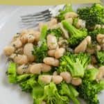 A plate of broccoli and white bean salad garnished with herbs, served with a fork; text reads "broccoli white bean salad" and "easy lunch recipe.