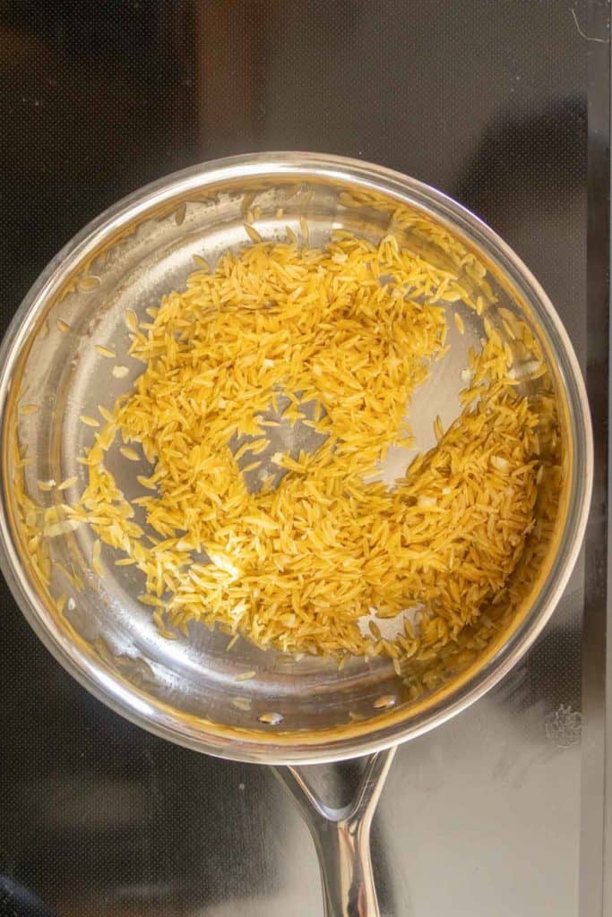 Uncooked rice being toasted in a stainless steel pan on a stovetop.