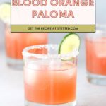 A glass of blood orange Paloma with a salted rim and a lime wheel garnish; two similar drinks are blurred in the background.
