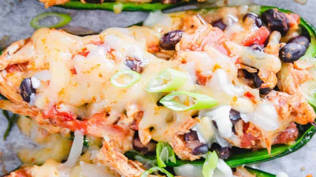 Close-up of stuffed peppers filled with shredded chicken, black beans, diced tomatoes, and melted cheese, topped with sliced green onions.