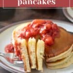 A plate of ricotta pancakes topped with strawberry sauce, with a fork holding a cut piece.