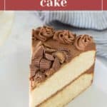 A slice of peanut butter cake with chocolate frosting and peanut butter cup pieces on a white plate.