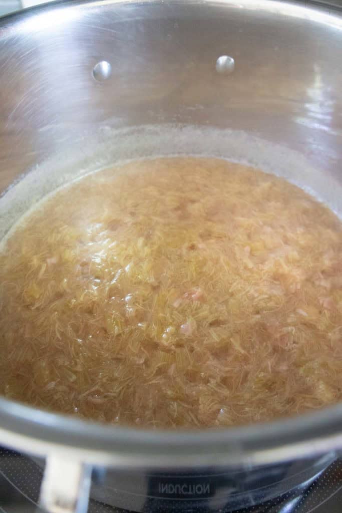 A pot of simmering rhubarb mixture with chopped pieces and liquid visible, as it cooks on a stovetop.