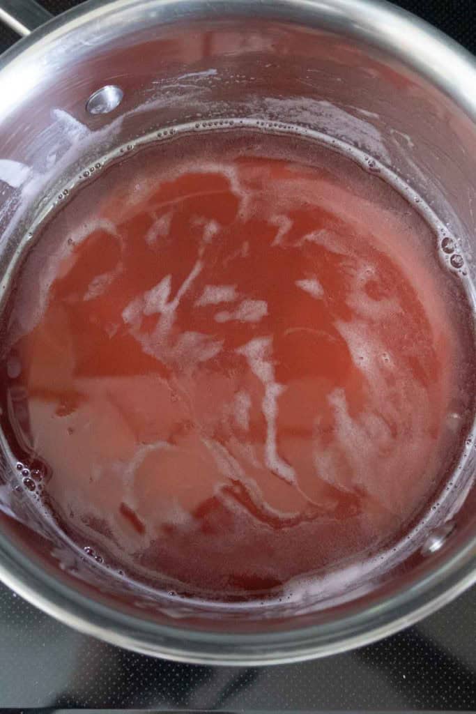 A stainless steel pot filled with a reddish liquid and some foam on the surface, placed on a stovetop.