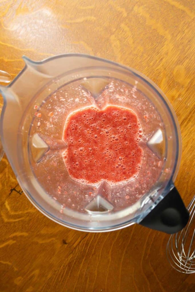 A blender containing a pinkish-red blended liquid sits on a wooden surface.