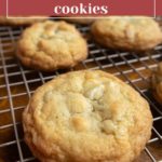 White chocolate macadamia nut cookies cooling on a metal wire rack, with a label at the top describing the cookie flavor.