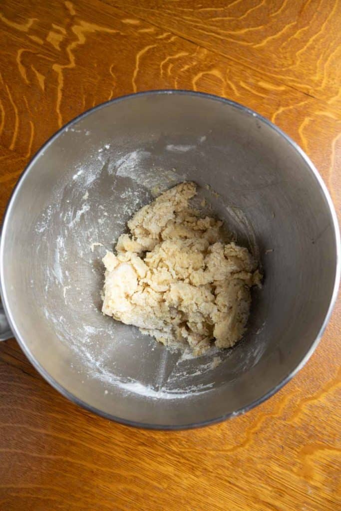 A stainless steel mixing bowl containing partially mixed dough sits on a wooden surface.