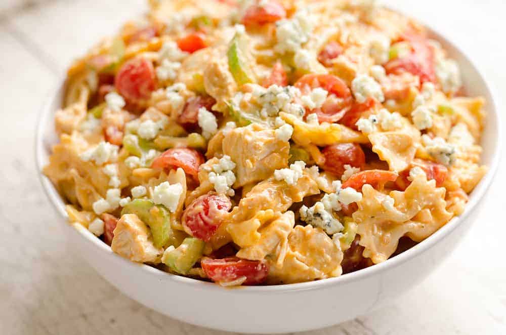 A white bowl filled with pasta salad containing bowtie pasta, cherry tomatoes, celery, diced chicken, crumbled blue cheese, and a creamy dressing.