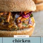Close-up of a chicken burger on a whole wheat bun, topped with colorful slaw and drizzled with peanut sauce.