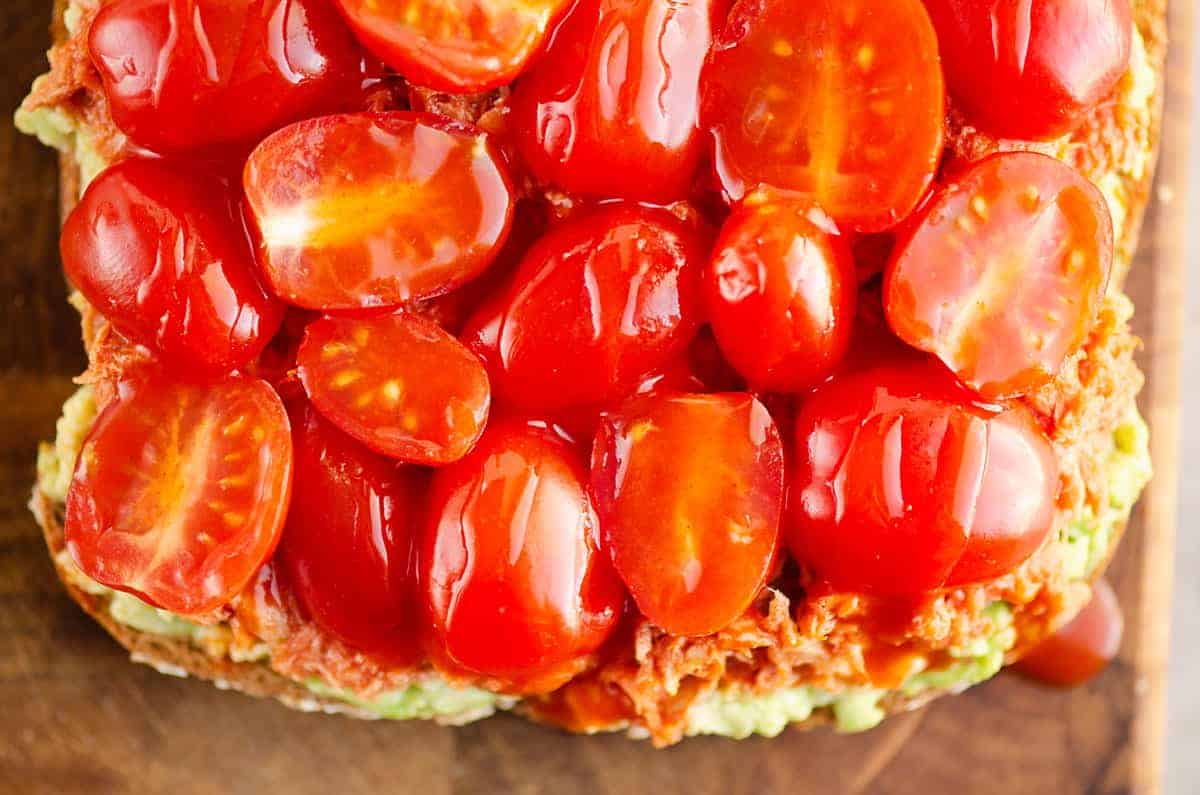 Close-up of sliced cherry tomatoes on top of mashed avocado spread over bread.
