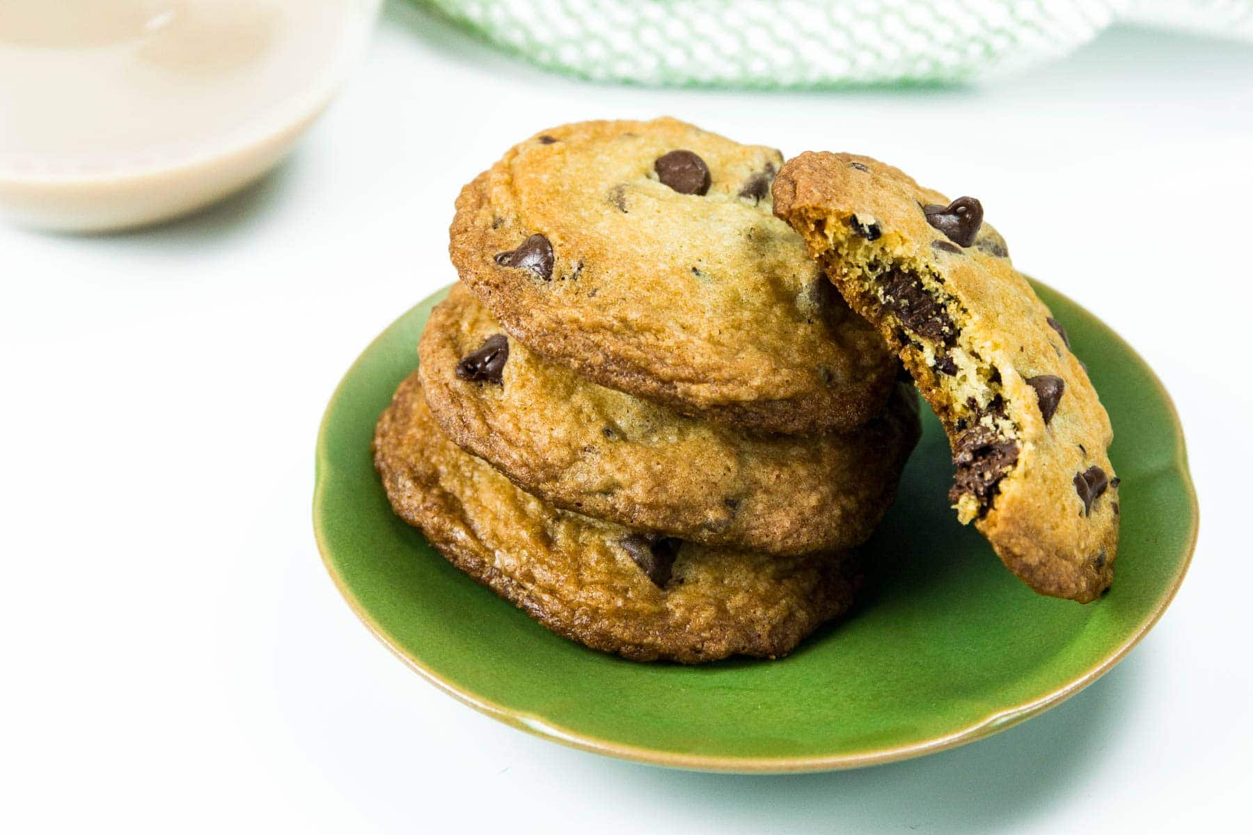 A stack of chocolate chip cookies on a green plate, with one cookie broken in half showing the chocolate chips inside.