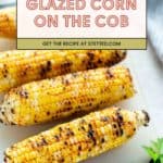 Three grilled corn on the cob pieces with a glazed coating are arranged on a white cutting board, garnished with parsley.