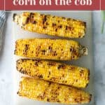 Four grilled ears of corn on the cob with visible char marks are arranged on a white cutting board. Text overlay reads "spicy glazed corn on the cob.