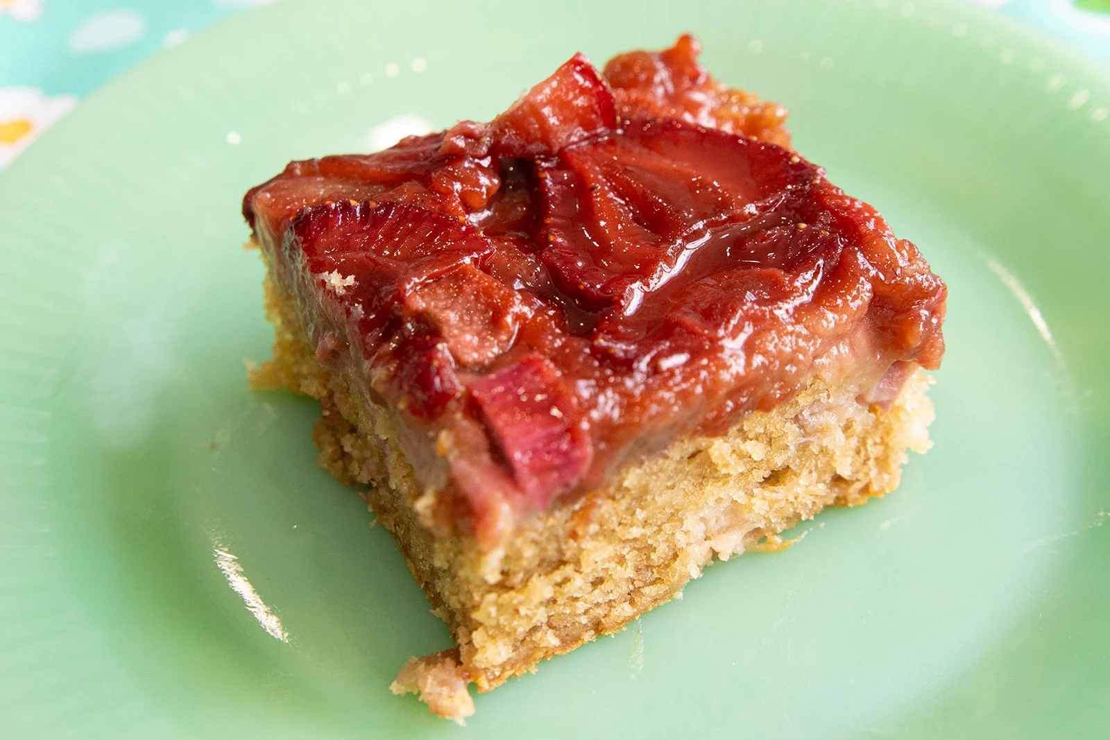A square slice of rhubarb and strawberry upside-down cake on a green plate.