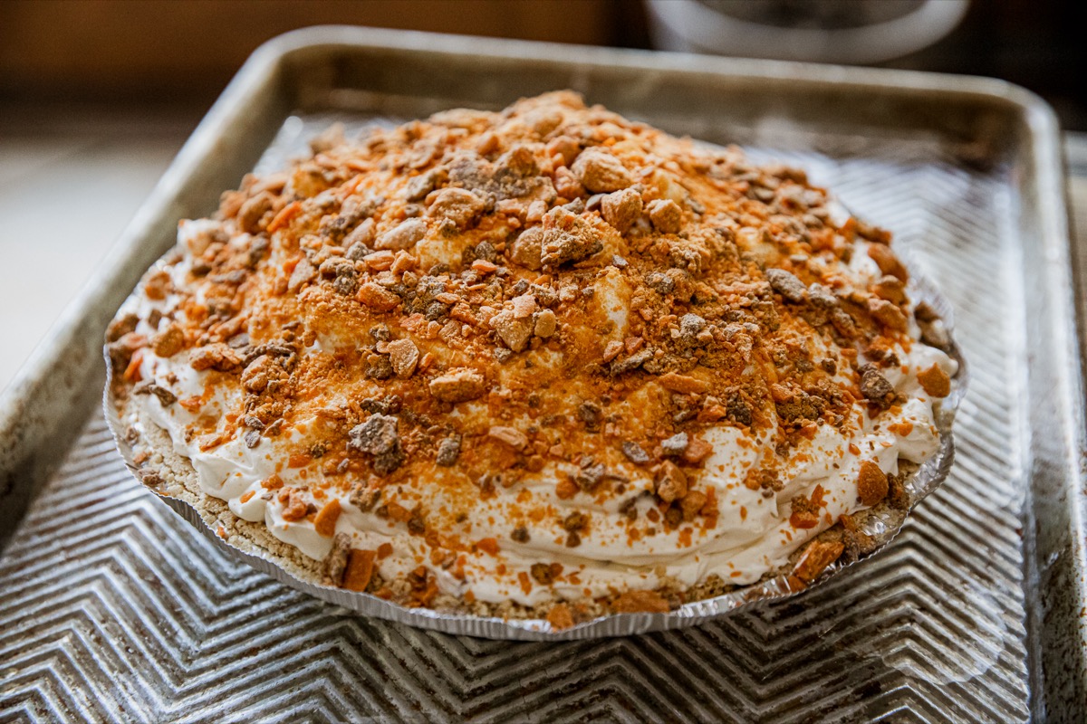 A pie topped with whipped cream and crushed cookies sits on a metal baking tray with a textured zigzag pattern.
