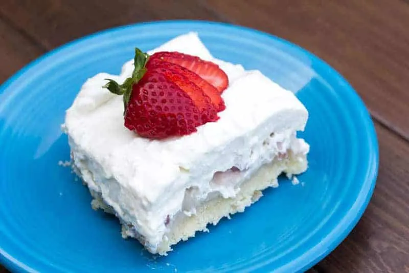 A square slice of creamy dessert topped with two strawberry slices, served on a blue plate.