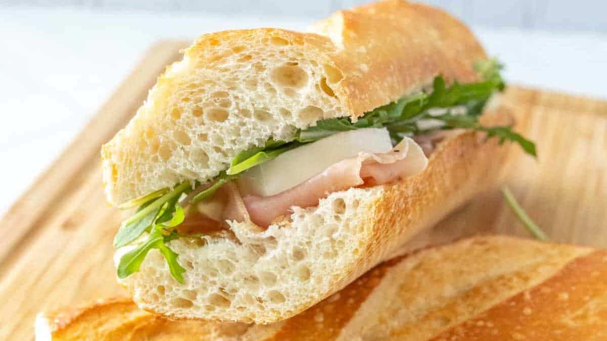 A sandwich with prosciutto and arugula on a wooden cutting board.
