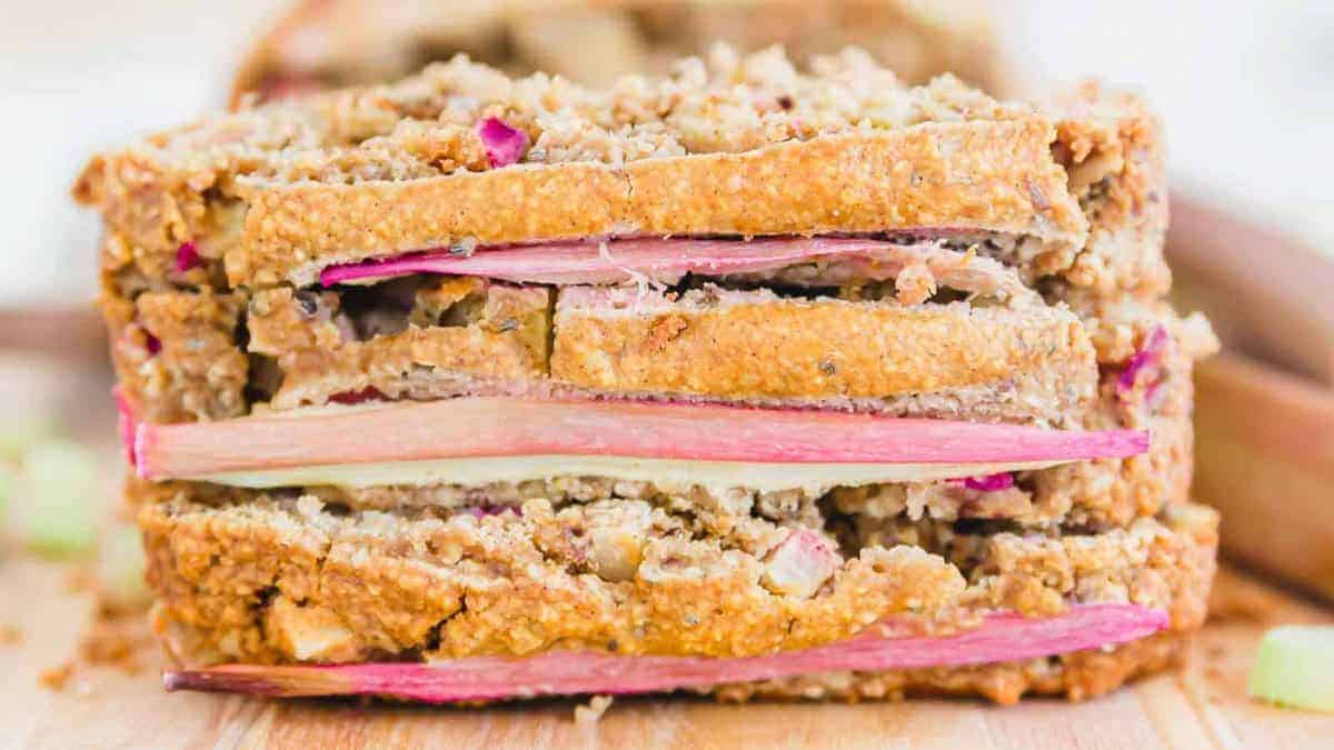 A close-up of thick slices of bread with visible pieces and layers of rhubarb inside, resting on a wooden surface.