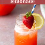 A mason jar filled with strawberry lemonade, garnished with a lemon slice and whole strawberry, with a blue and white striped straw.