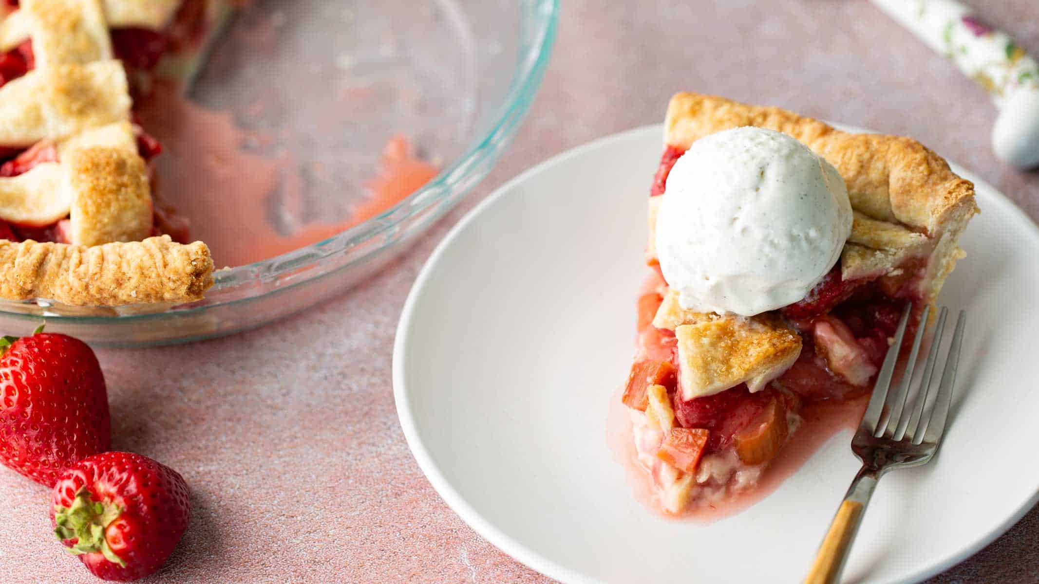 A slice of strawberry rhubarb pie on a plate with ice cream on top.