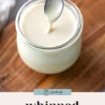 A spoon dipped into a jar of whipped honey, placed on a wooden surface.