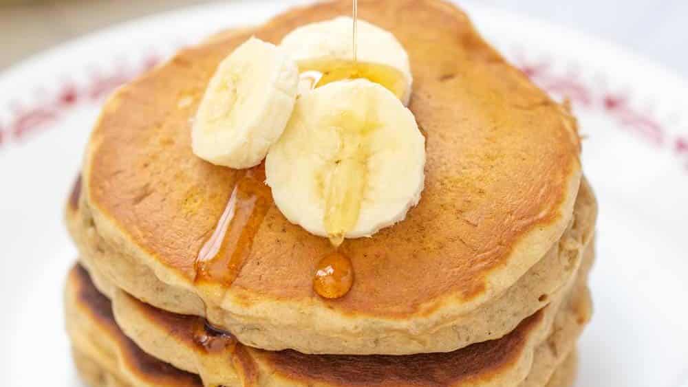 syrup being poured onto banana bread pancakes