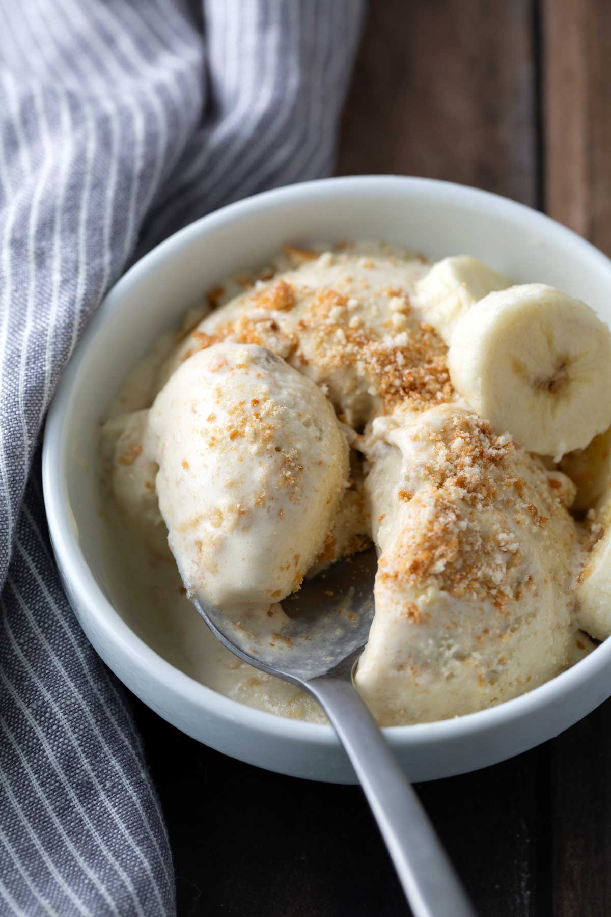 A bowl of banana pudding topped with crushed cookies and banana slices, with a spoon resting inside.