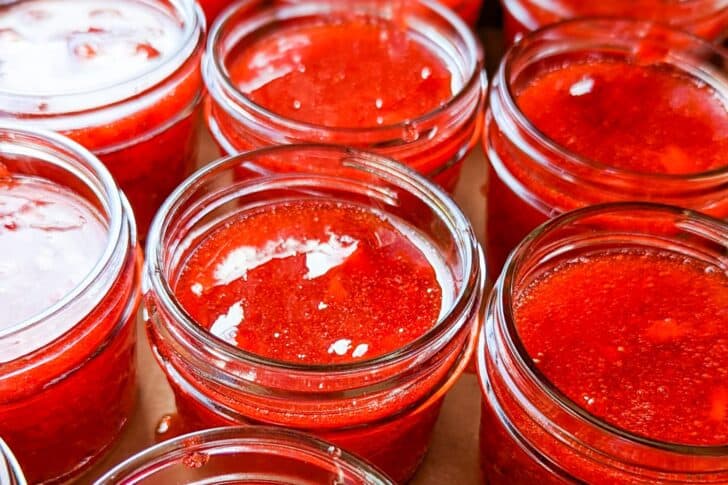 Close-up view of several open glass jars filled with bright red strawberry jam.